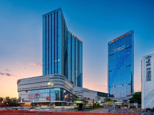 a large glass building in front of two tall buildings at Hilton Garden Inn Taiyuan Binhe in Yangjiabu