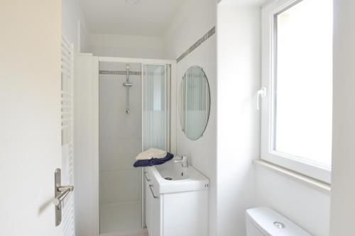 une salle de bain blanche avec des toilettes et un lavabo dans l'établissement L'Écrin de Douvres - Charmante maison pour 2p, à Douvres-la-Délivrande