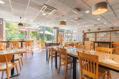 un restaurant avec des tables et des chaises en bois et des fenêtres dans l'établissement Appart’City Confort Lyon Cité Internationale, à Caluire-et-Cuire