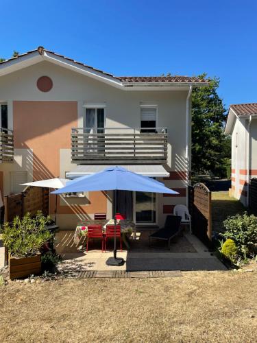 une terrasse avec un parasol bleu et des chaises ainsi qu'une maison dans l'établissement Rêves d'Océan villa familiale calme bord de mer piscine partagée surf, à Soulac-sur-Mer
