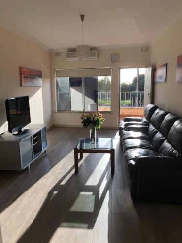 sala de estar con sofá de cuero negro y TV en Beach side holiday unit, en Port Adelaide