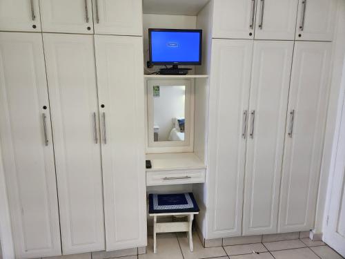 a room with white cabinets with a tv and a desk at Driftsands Sea View Flats in Uvongo Beach