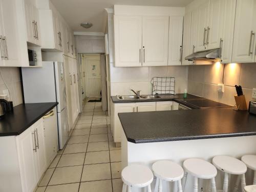 a kitchen with white cabinets and white stools at Driftsands Sea View Flats in Uvongo Beach