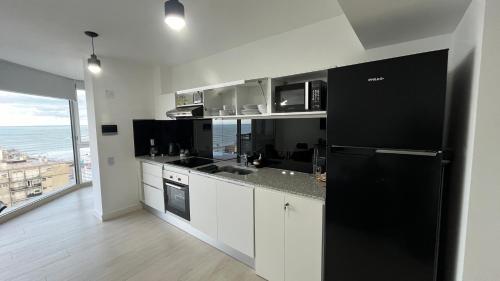 a kitchen with a black refrigerator and a large window at Excelente! Vista al mar con cochera y amenities gimnasio, play room y pileta no climatizada in Mar del Plata