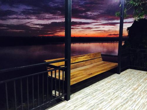 a wooden bench overlooking a lake with a sunset at Mekong Tarawadee Villa in Tha Bo