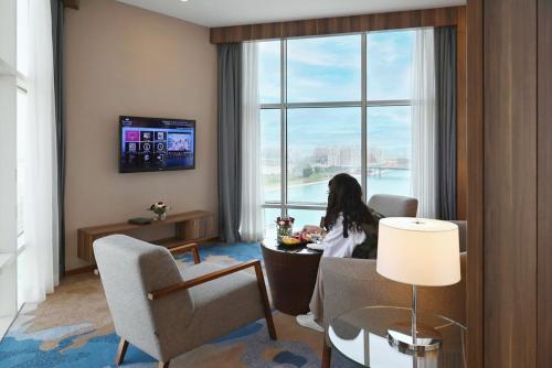 a woman sitting in a room with a large window at Bay La Sun Hotel and Marina - Emaar King Abdullah Economic City in King Abdullah Economic City