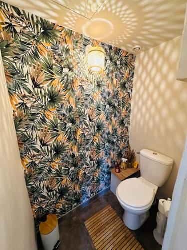 une salle de bain avec toilettes et un papier peint tropical dans l'établissement Charmant Appartement T4, à Le Teil