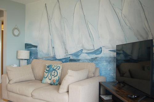 a living room with a couch and a painting of sailboats at Sound of the Sea, beach front Bungalow with hot tub, in Tywyn in Tywyn