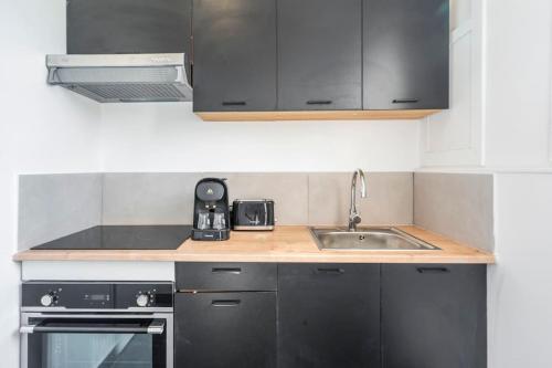 - une cuisine avec des placards noirs et un évier dans l'établissement Studio paisible en banlieue parisienne - Montreuil, à Montreuil