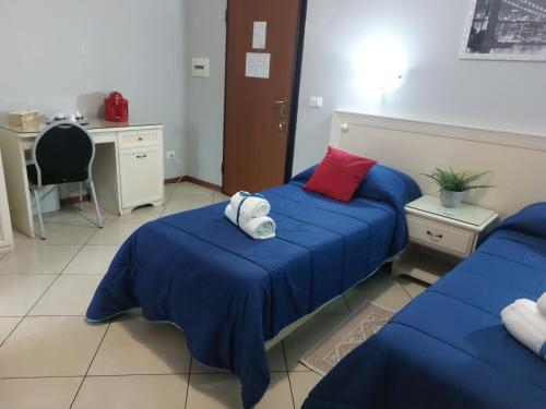 a room with two beds with blue sheets and a desk at Fiumicino Inn Airport in Fiumicino