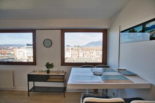 une table et des chaises dans une pièce avec deux fenêtres dans l'établissement Le sommet citadin avec vue, à Annecy