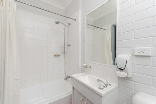 Baño blanco con lavabo y espejo en Herston Place Motel, en Brisbane