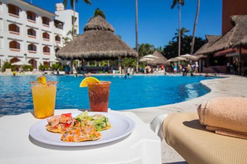 a plate of food and a drink on a table next to a pool at Plaza Pelicanos Club Beach Resort All Inclusive in Puerto Vallarta