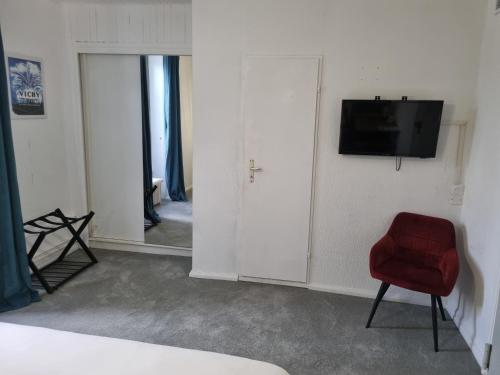 a room with a red chair and a television on a wall at Hôtel & Restaurant Le Patio VICHY in Vichy