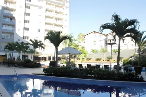 a swimming pool with palm trees and a building at Apartamentos em Rio Quente com maravilhosa área de lazer e excelente localização in Rio Quente