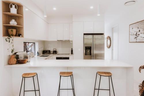 a kitchen with white cabinets and two bar stools at Contemporary Coolum Beach Abode in Coolum Beach
