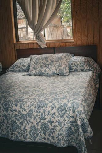 a bed with a blue and white comforter and a window at Cabaña Santa Amelia Antuco Pet Friendly in Peluca