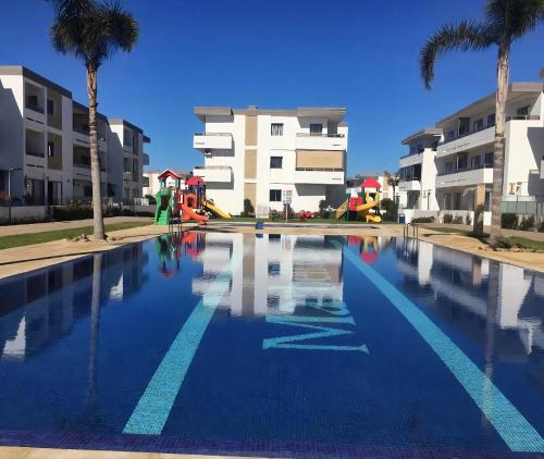 a large swimming pool with palm trees and buildings at Marbella beach appart de standing in Mansouria
