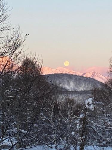a full moon rising over a snowy mountain with trees at Madarao Lainstons in Iiyama