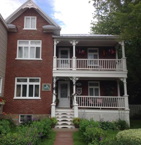 a large red brick house with a white balcony at La Belle Visite, anciennement Gîte Victoria in Rimouski