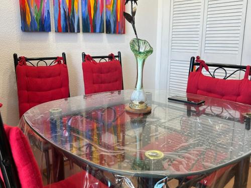 une table en verre avec un vase dessus avec des chaises rouges dans l'établissement Studio climatisé à 300m de la plage avec parking et terrasse - Argelès-sur-Mer - FR-1-732-84, à Argelès-sur-Mer