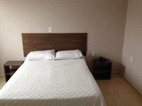 - une chambre avec un lit blanc et une tête de lit en bois dans l'établissement Hotel Cedro Palace, à São José do Cedro