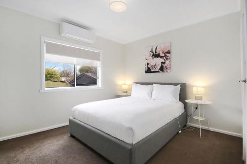 a white bedroom with a bed and a window at Lake Reflections in Beechworth