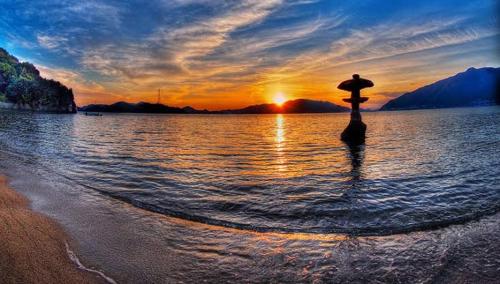 a person standing in the water on the beach at sunset at Beach Villa Tachibana in Onomichi
