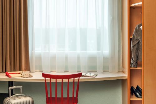 a red chair sitting in front of a desk with a window at ibis Luebeck City in Lübeck