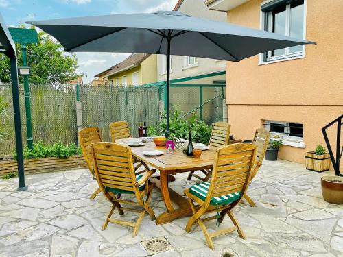 a wooden table with chairs and an umbrella on a patio at Maison Calme et Confort avec Jardin, Face Parc Exposition - Aéroport du Bourget, à 10 min de CDG in Le Blanc-Mesnil