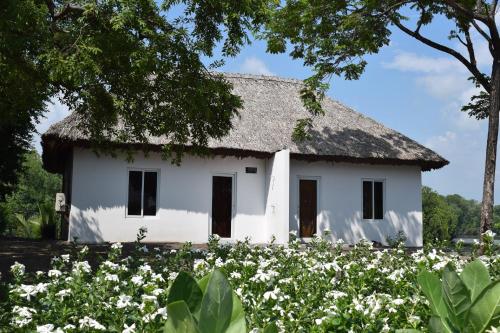 a white house with a thatched roof and a field of flowers at Hotel Maya Jade in Monterrico