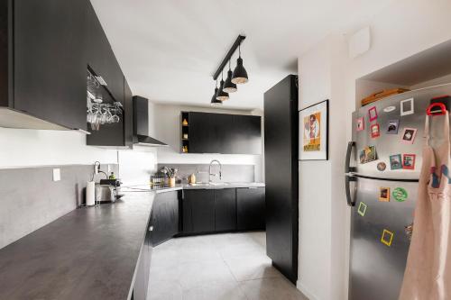 - une cuisine avec des armoires noires et un réfrigérateur dans l'établissement Urban Comics - Appt climatisé 10p proche de Paris, à Brétigny-sur-Orge