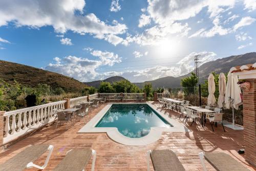 ein Pool mit Stühlen und Tischen auf einer Terrasse mit Bergen in der Unterkunft MalagaSuite Casa Rural Alcaucin in Alcaucín