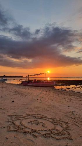 a boat on the beach with the sunset in the background at Uncle Hippie's Dream in Gili Meno