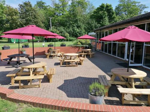 a patio with picnic tables and umbrellas in front of a building at Manor Of Groves Hotel, Golf & Health Club in Sawbridgeworth
