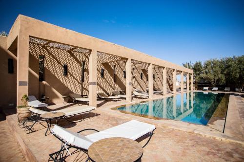 a swimming pool with chairs and tables on a patio at Kanz Erremal in Merzouga