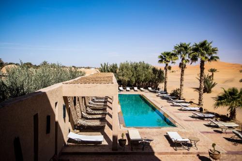 a resort with a swimming pool and chairs and palm trees at Kanz Erremal in Merzouga