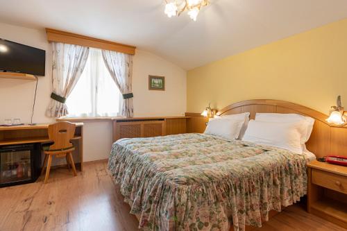 a bedroom with a bed and a desk and a window at Hotel Patrizia Dolomites Glamour in Moena