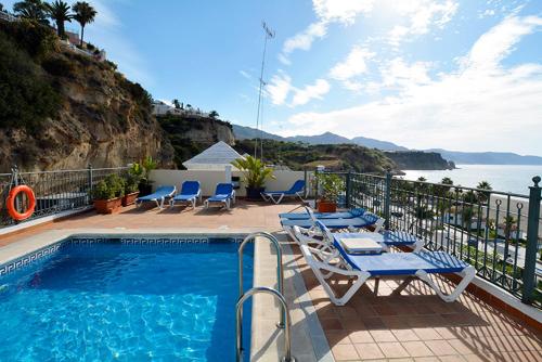 a swimming pool with chairs and a table and the ocean at Apartamentos HC Burriana Playa in Nerja