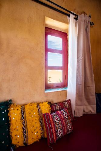 a couch with colorful pillows in front of a window at Kanz Erremal in Merzouga