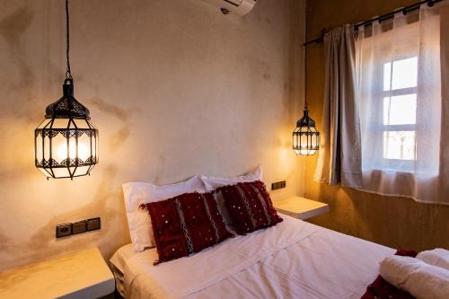 a bedroom with a bed and two lights and a window at Kanz Erremal in Merzouga