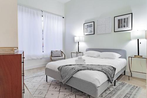 a white bedroom with a bed and a chair at Vibrant 2-BR Luxe Flat Adjacent Eastern Market Walk to METRO Barracks Row Capitol Hill in Washington, D.C.