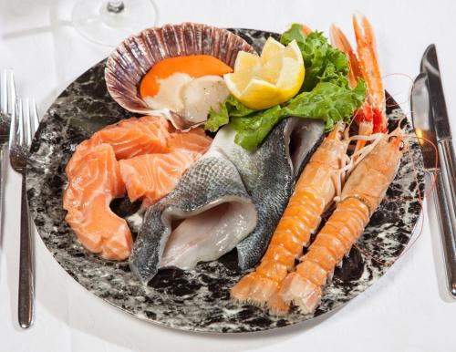 a plate of food with fish and vegetables on a table at Hotel Comfort Erica Dolomiti Val d'Adige in Salorno sulla Strada del Vino
