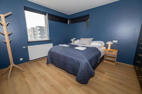 a blue bedroom with a bed and a window at Family apartment hosted by LL in Akureyri