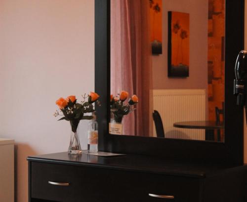 a dresser with a mirror and vases with orange flowers at Enastron Hotel in Kato Loutraki