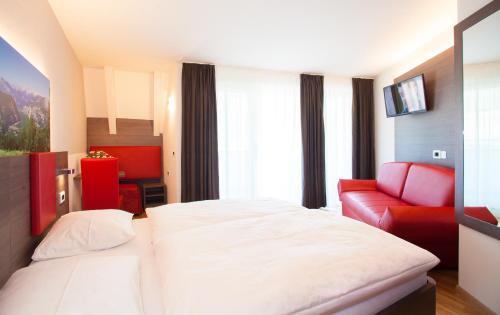 a hotel room with a bed and a red couch at Hotel Comfort Erica Dolomiti Val d'Adige in Salorno sulla Strada del Vino