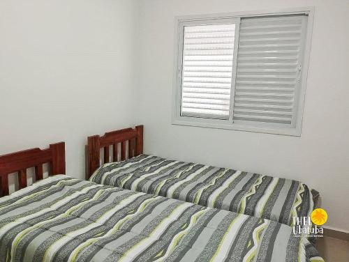 two beds in a bedroom with a window at Espaçoso, bem equipado AR e piscina Climatizada in Ubatuba