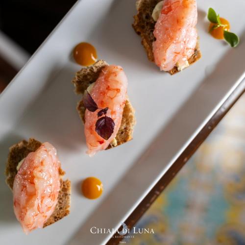 a white plate with three pieces of shrimp on it at Hotel Chiaia Di Luna in Ponza