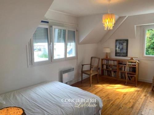 a bedroom with a bed and a chair and windows at Frangipanie in Urville-Nacqueville