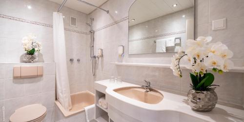 a white bathroom with a sink and a vase of flowers at PLAZA INN Rieker Stuttgart Hauptbahnhof in Stuttgart